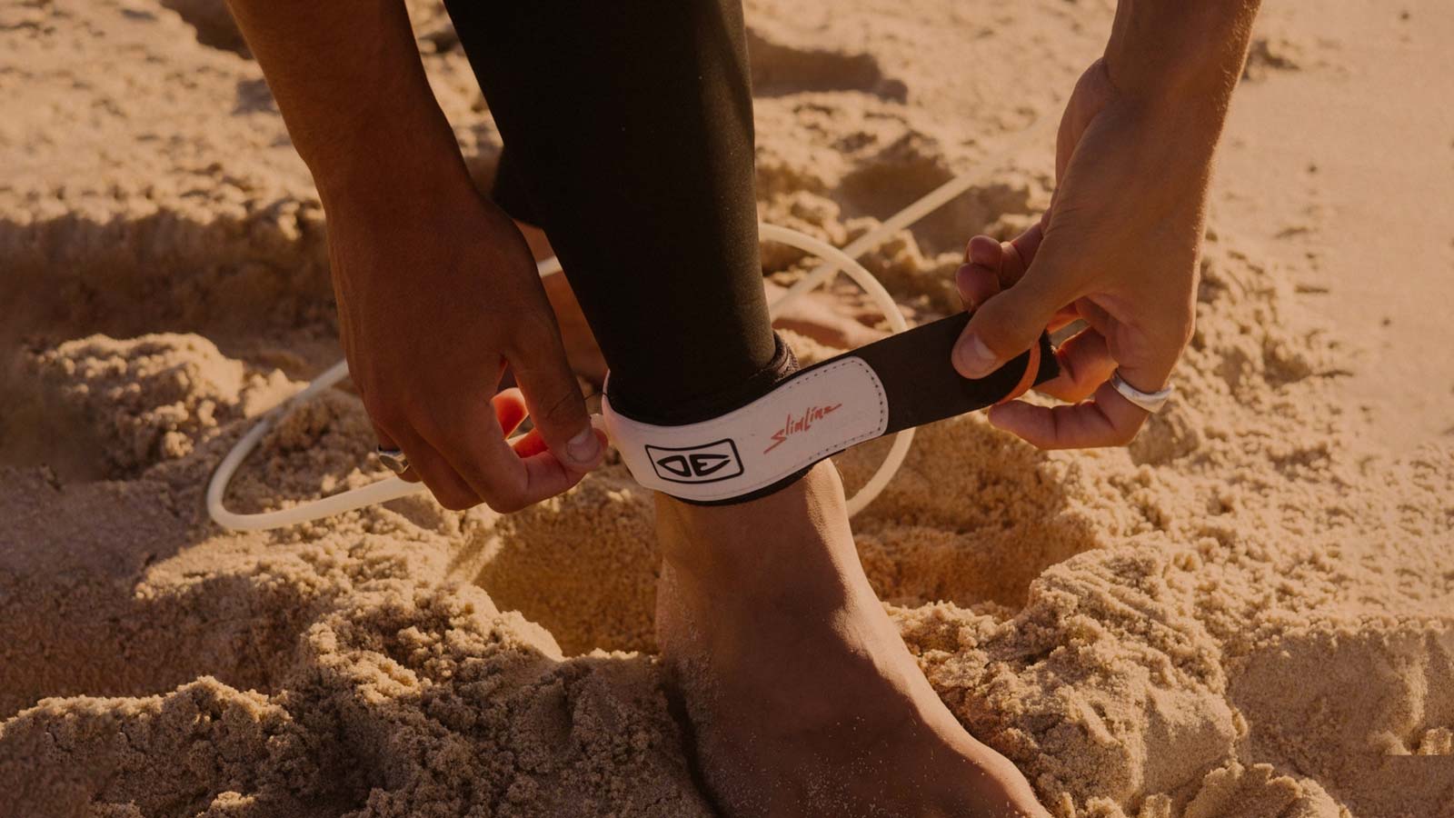 Surfboard leash getting wrapped around leg. Sandy beach.