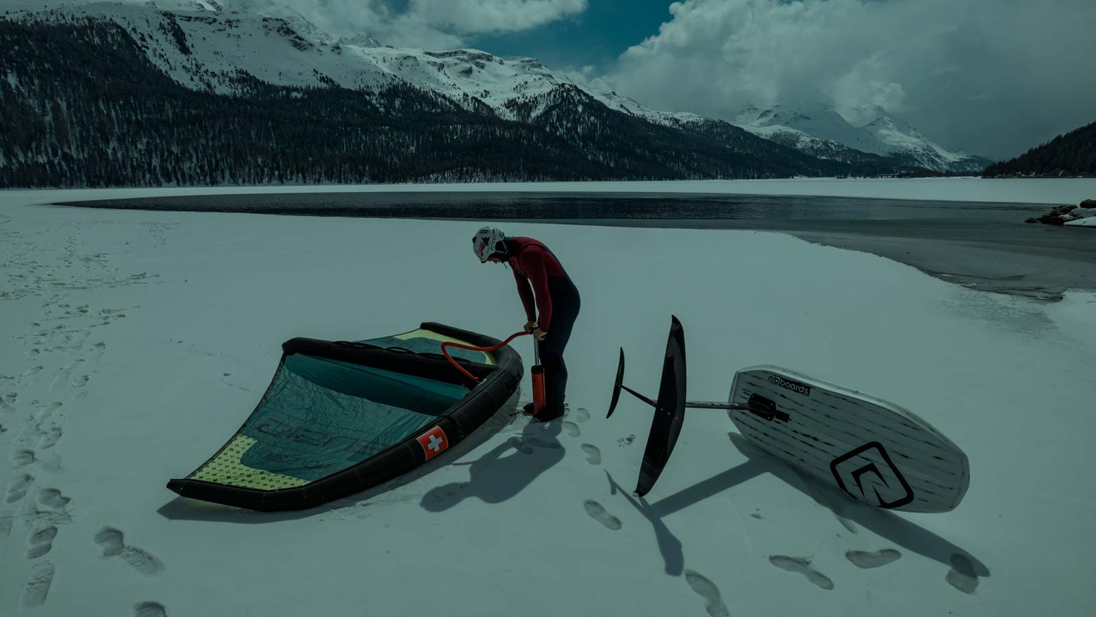 Athlete pumping his wing. Hydrofoil board next to him ready for a ride.