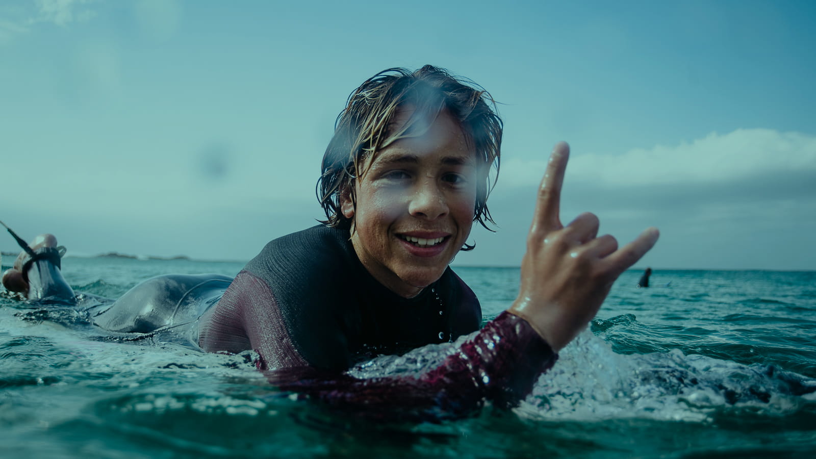 Happy kid in warm wetsuit waiting for the wave and waving to the camera. 