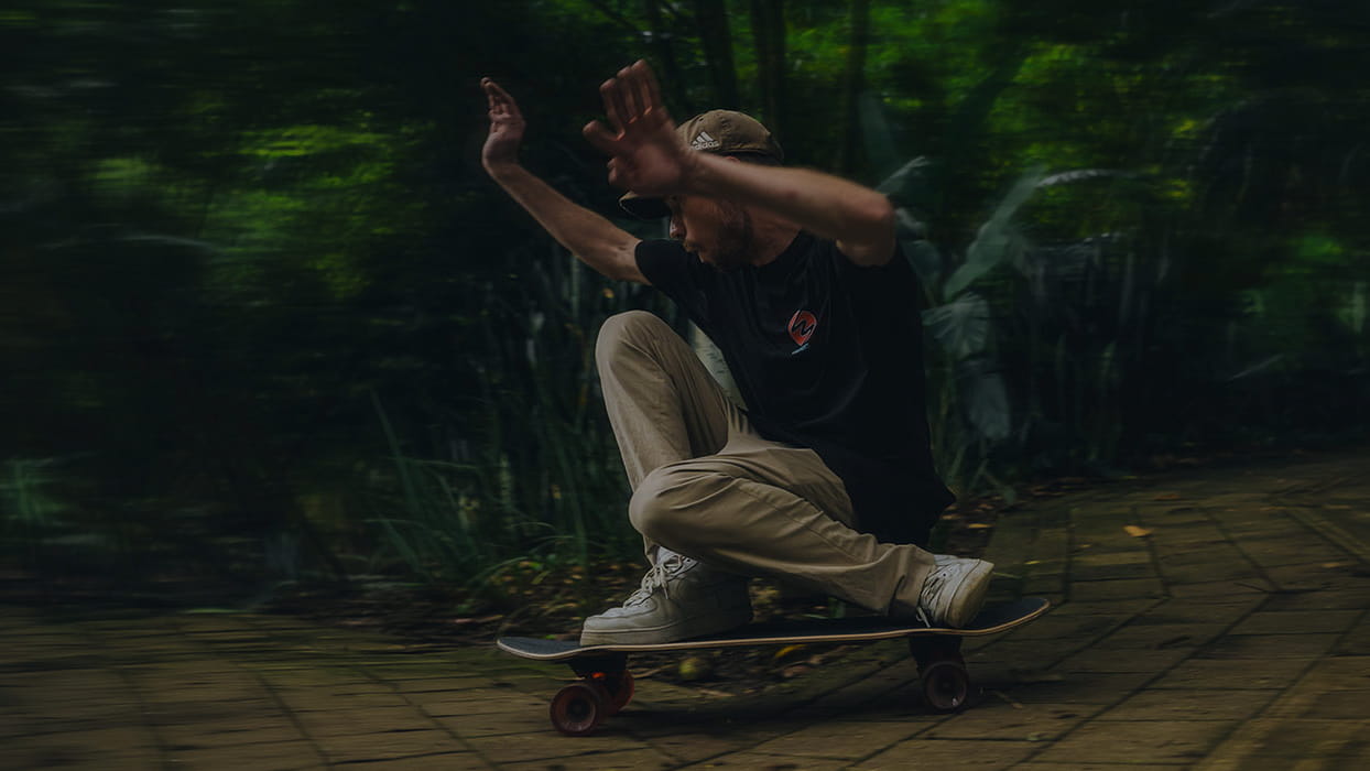 Skatboard with cruiser skatboard charging trough the corner. Green garden.  