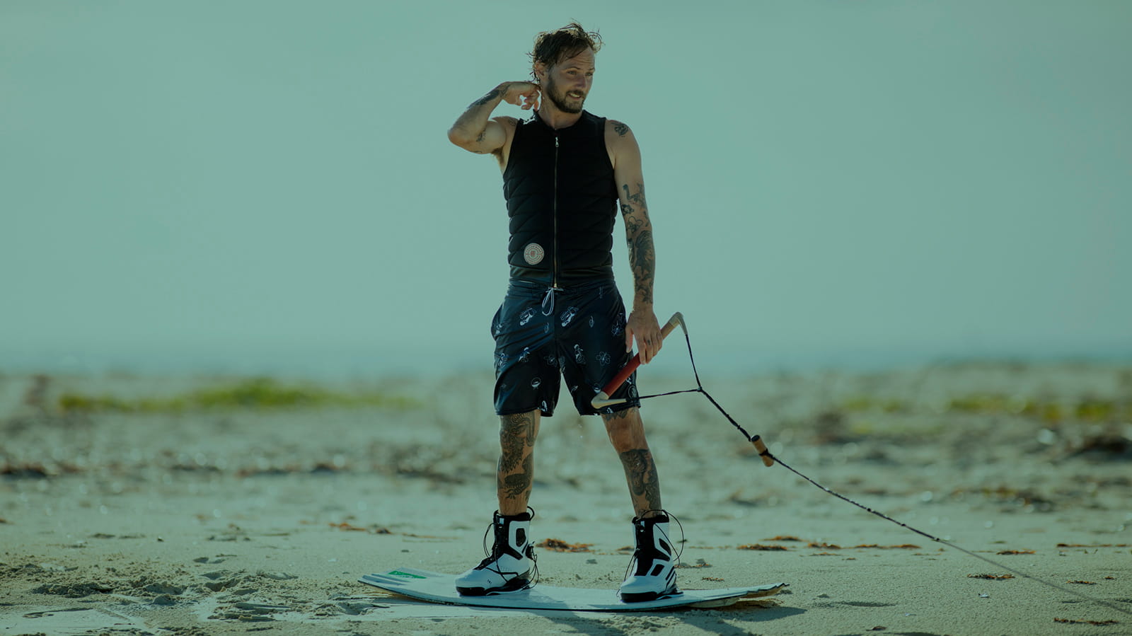 Men's Life Jackets and Impact vests. Wakeboarder waiting for the pull standong on the board with a handle in hands.