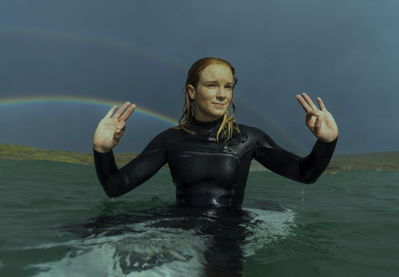 Women sitting on a surfboard and waiting for waves to come. Rainbow in the background.